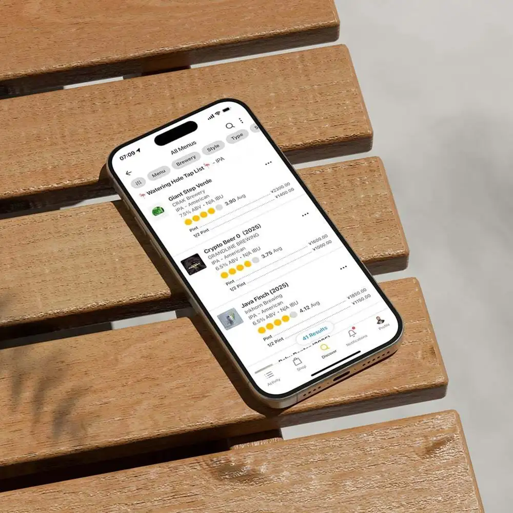 A phone sitting on a wooden park bench, showing the Untappd app and a menu